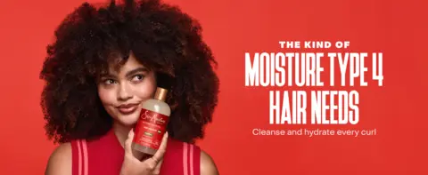 A woman with voluminous curls holds a SheaMoisture bottle against a bold red backdrop.