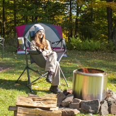 Young smiling woman sitting with crossed legs in swing chair by a campfire