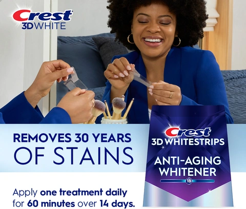 Reflection of woman in mirror smiling and peeling a Crest 3DWhitestrip. Removes 30 Years of Stains.