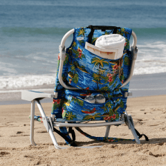 Back of a beach chair with towel rolled up in zippered pockets on the beach.  