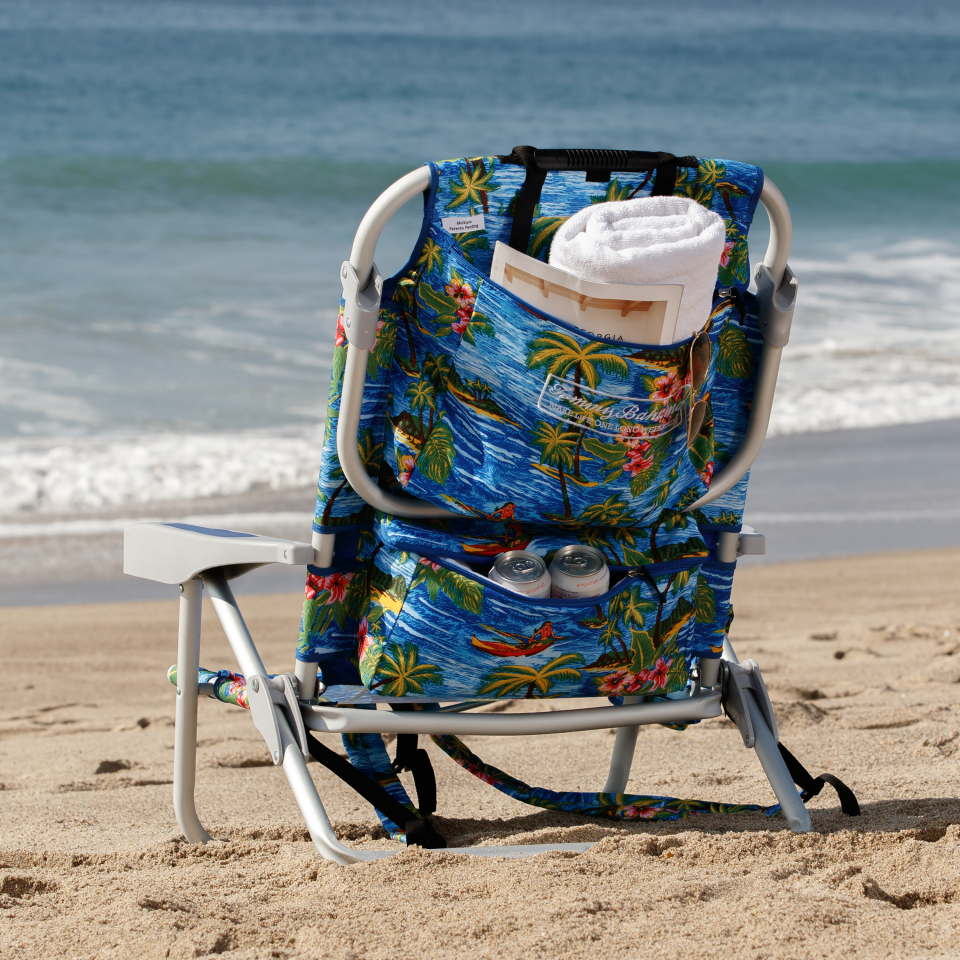 Back of a beach chair with towel rolled up in zippered pockets on the beach.  