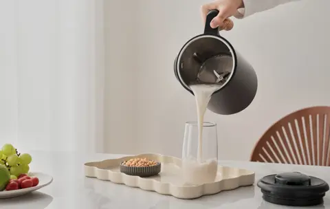 A person pouring a beverage out of the nut milk maker.