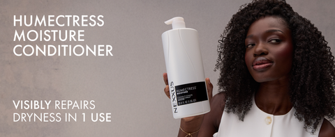 Young woman with healthy curly dark hair holding a Nexxus Therappe Moisture Conditioner bottle.