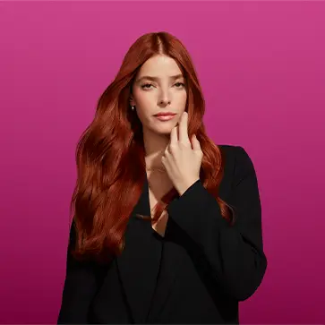 Image of same woman with auburn hair dressed in black and raising her left hand to touch her healthy, vibrant hair.