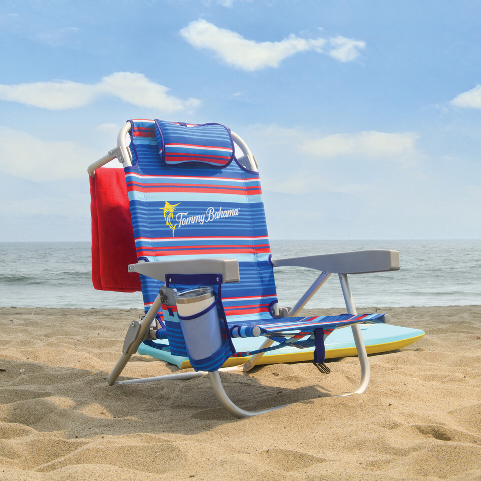 Beach chair on the beach with towel on towel bar on back of chair.