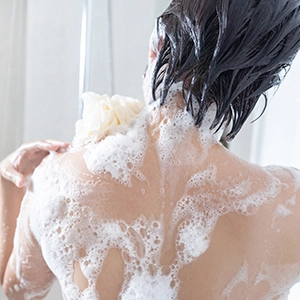 A person in the shower facing away from the camera with foamy soap on their back and neck.