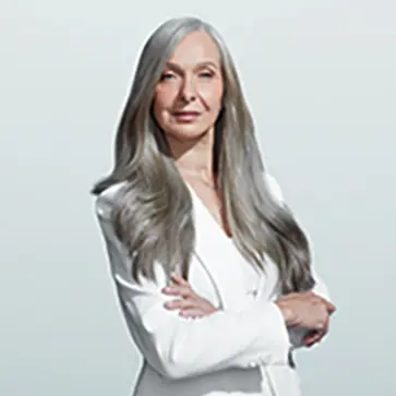 A portrait of a light-skinned woman with long, healthy, silver hair wearing a white blousse.