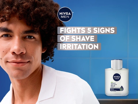 "Man with curly dark hair and NIVEA MEN Sensitive Post Shave Balm bottle against blue background, text reads Fights 5 Signs of Shave Irritation"