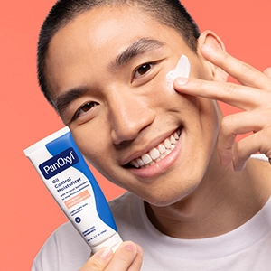 A young man holding a tube of Oil Control Moisturizer and applying some of the lotion to his cheek