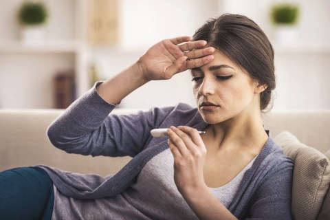 Woman with headache holding thermometer