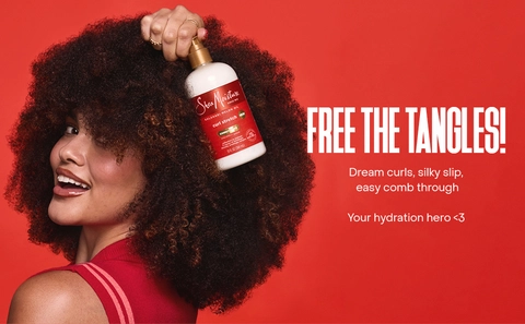 A woman with voluminous curls holds a SheaMoisture bottle against a bold red backdrop.